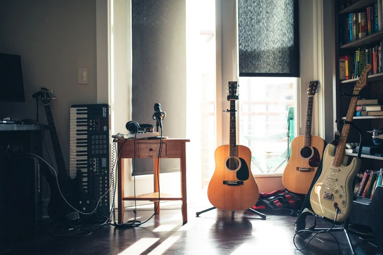 Guitars, a keyboard and a microphone sit in the corner of a room in front of a window