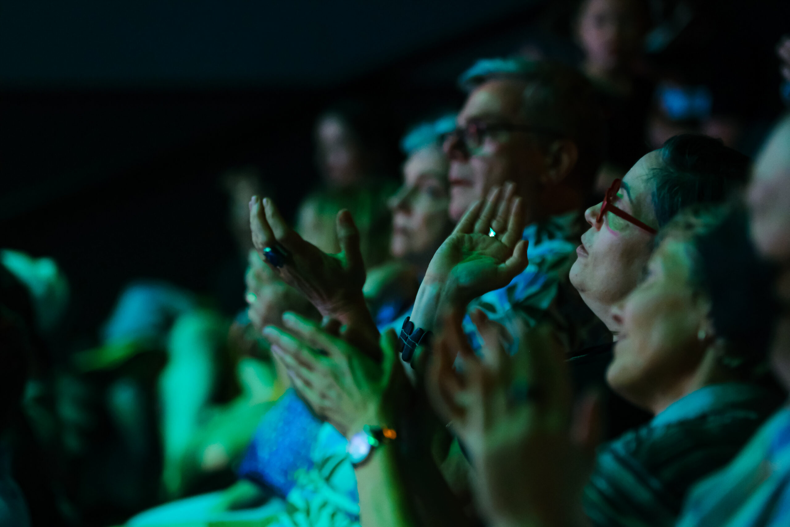 Close up of an audience clapping with their hands moving and faces looking upwards