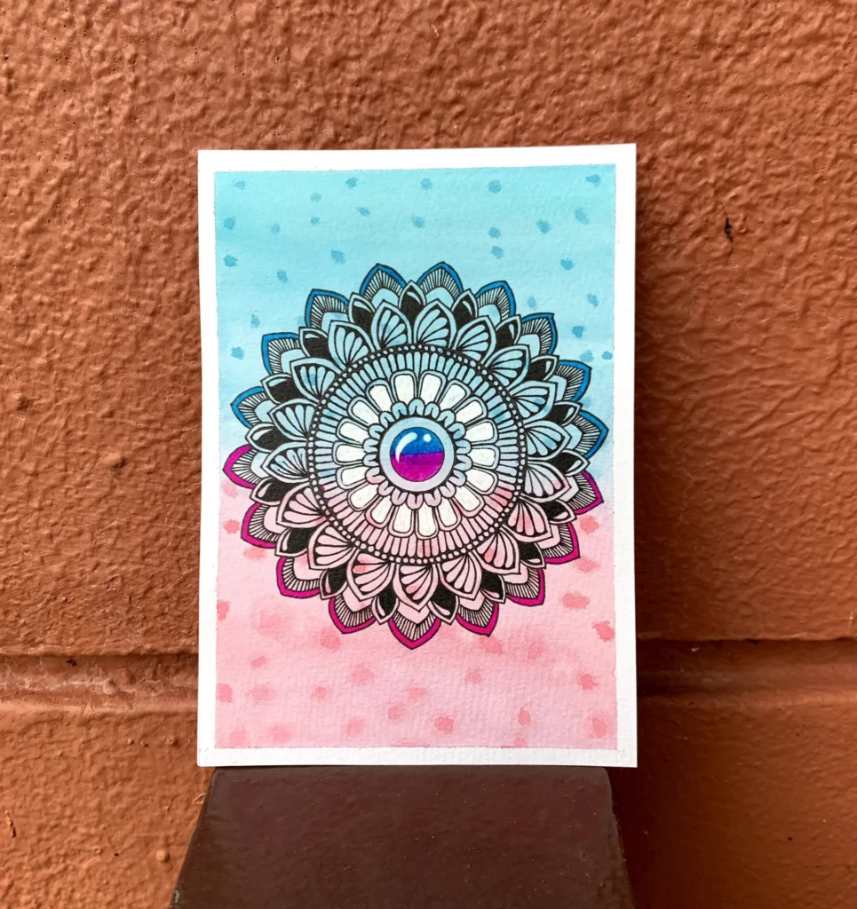 Picture of a black and white mandala pattern on a light blue and pink background