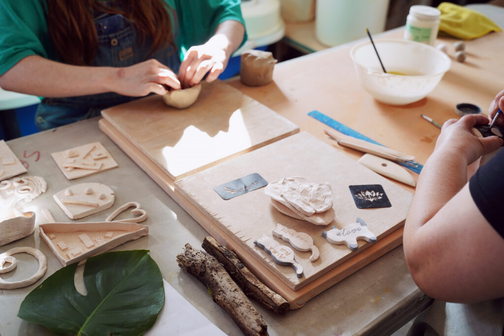 Close up view of a table with two people who are shaping small clay pots with clay tools on the table