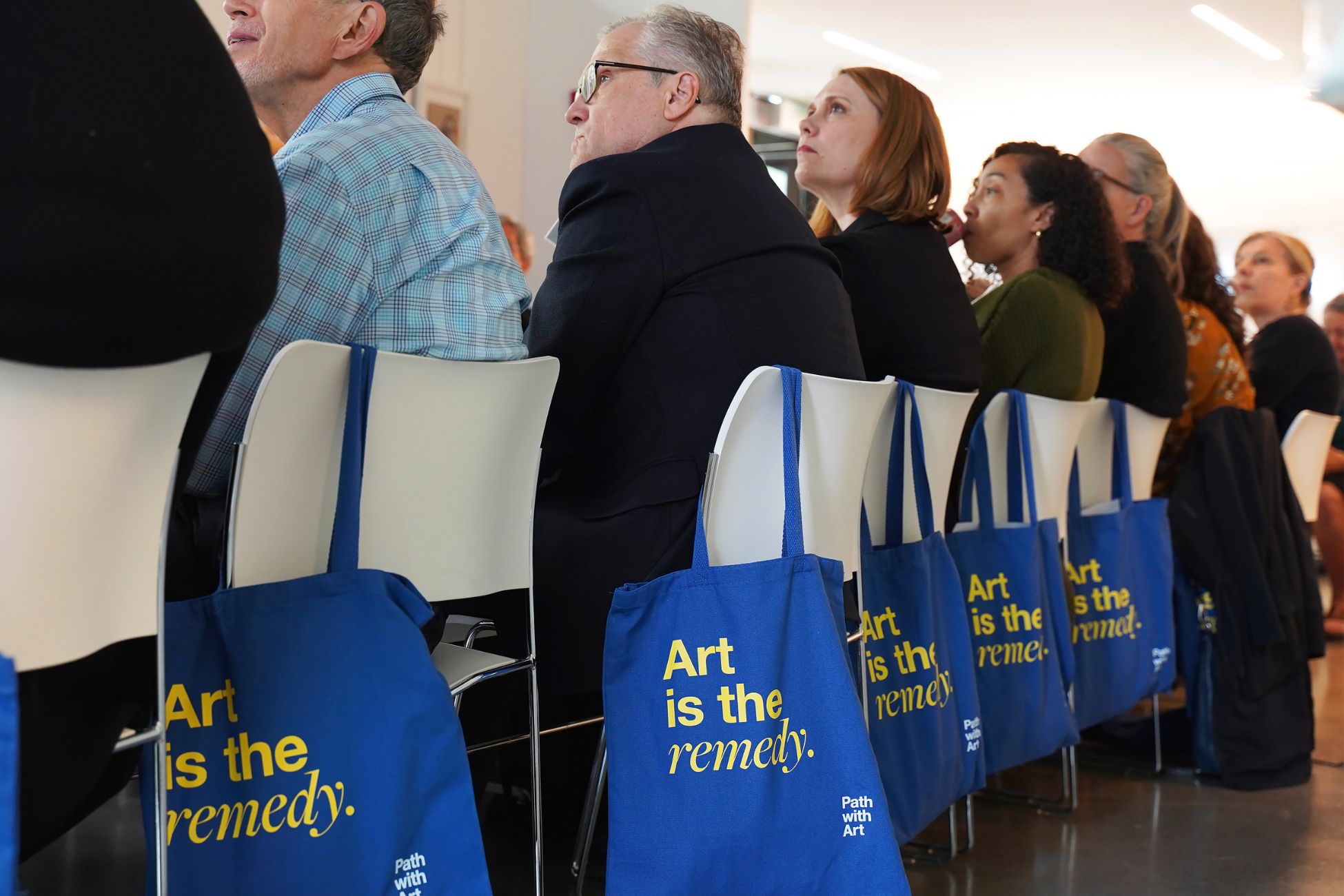 people sitting at a table with bags on their chairs that say art is the remedy